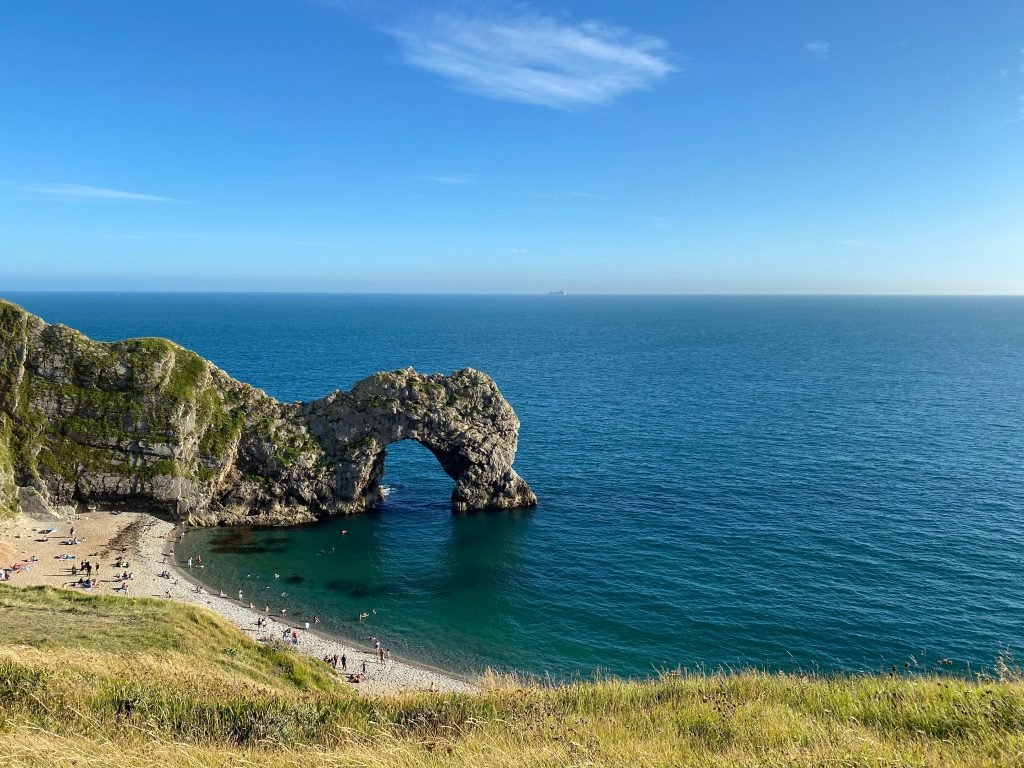 A breathtaking view of Durdle Door rock formation and beach under a clear blue sky, perfect for summer travel enthusiasts.