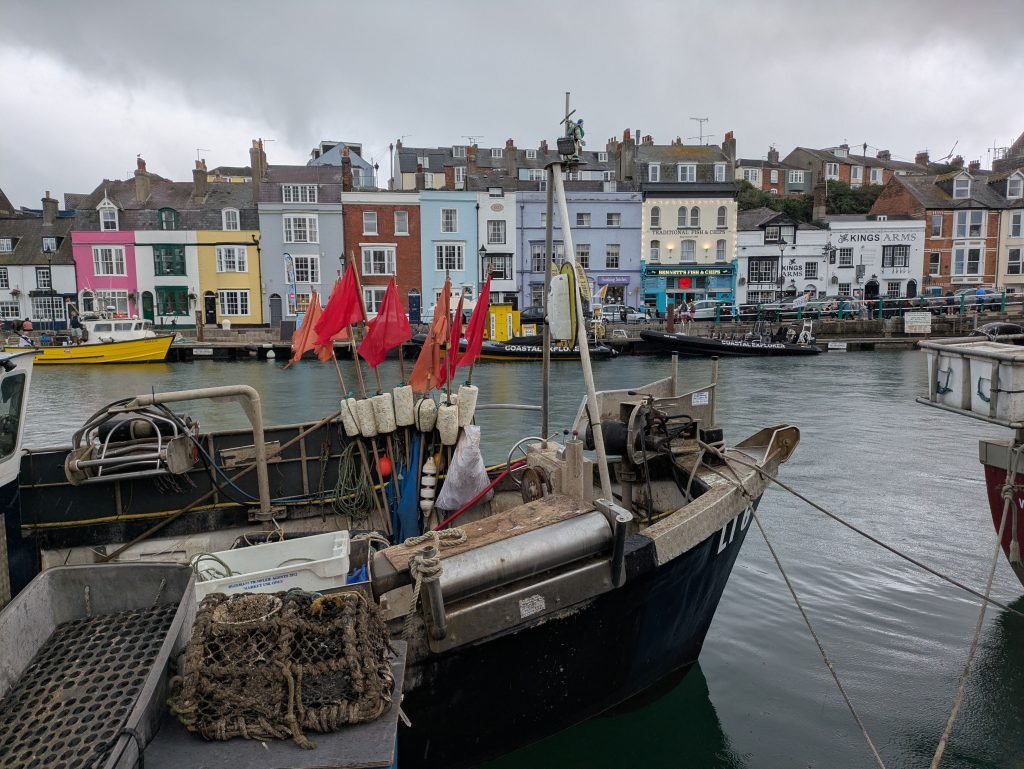 Fishing boats docked at Weymouth Harbour with colorful houses in the background, a vibrant coastal scene.